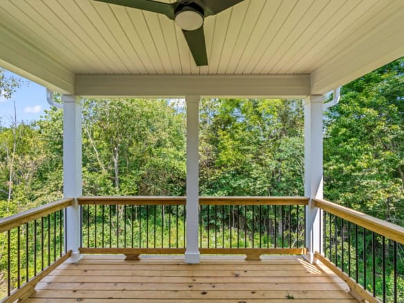 Porch with wooden railing overlooking a lush green forest.