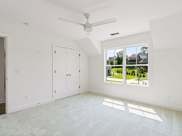 Bright, spacious bedroom with white walls and a large window overlooking a green yard.