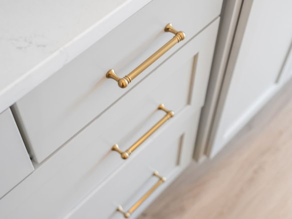 Close-up of light gray kitchen drawers with gold handles in a contemporary home.
