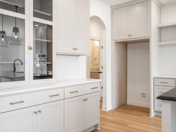 Bright white kitchen with built-in cabinets, open shelves, and hardwood flooring.