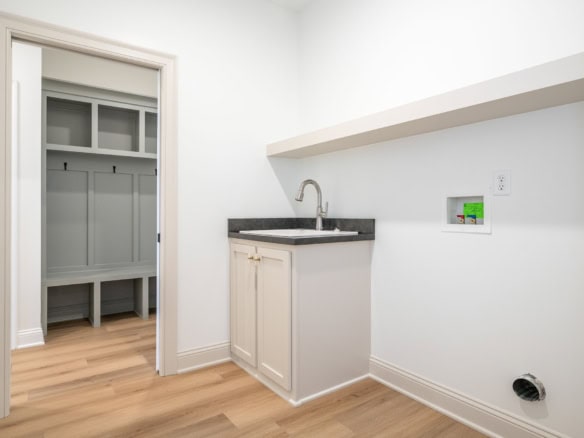 Modern laundry room with sink, white cabinets, and open closet space.
