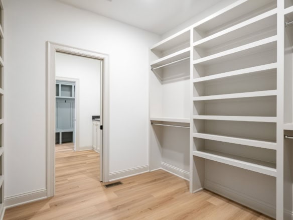 Walk-in closet with white shelving and wooden flooring.