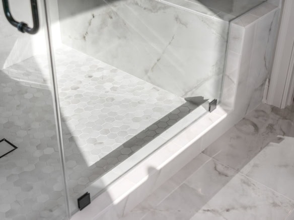 Glass shower with marble walls and hexagon tile floor.