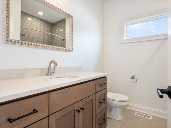 Bright bathroom featuring a wooden vanity, mirror, and small window.