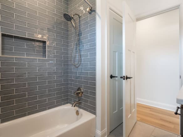 Bathroom with gray subway tile walls, showerhead, and bathtub.