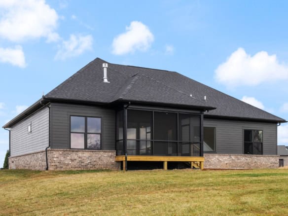 A house with gray siding, black roof, and screened porch on a grassy lot.