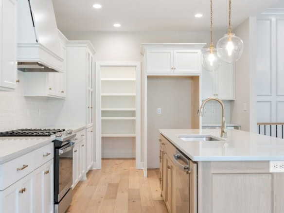 Image of a contemporary white kitchen with an island, pendant lights, and ample storage space.