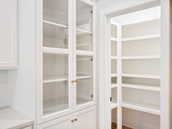 White built-in pantry with glass doors and shelving for storage.