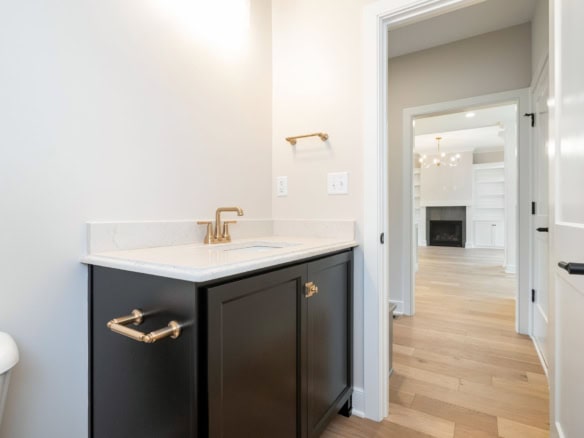 Interior view of a modern bathroom with a black vanity, white walls, and hardwood flooring.