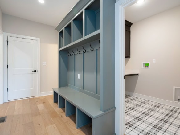 Interior view of a modern mudroom with built-in storage bench, hooks, and a plaid floor.