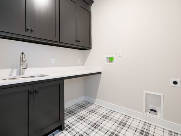Modern laundry room with black cabinets, white countertop, and checkered flooring.