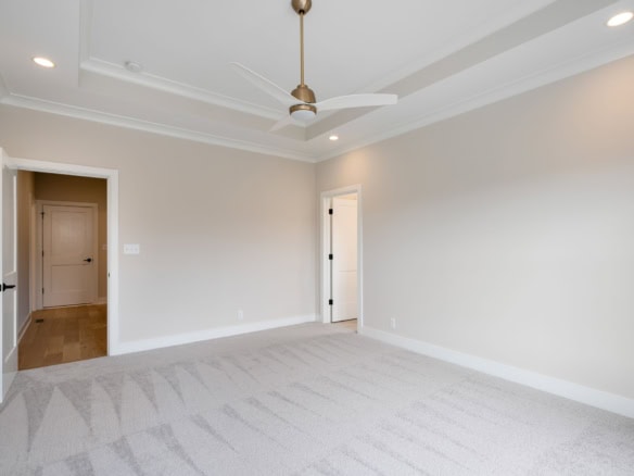Empty bedroom with neutral walls, ceiling fan, and natural light.