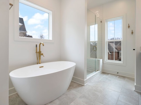 Bright bathroom featuring a white freestanding tub and glass shower with large windows.
