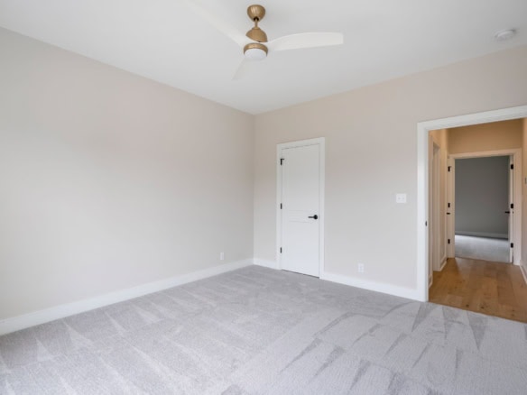 A bright, spacious bedroom with neutral walls, carpet flooring, and a ceiling fan.