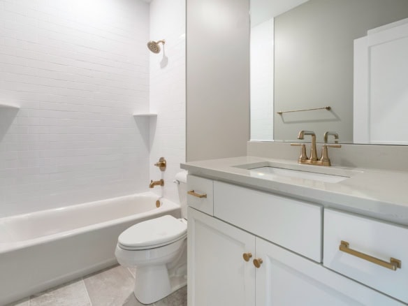 Bathroom with white bathtub, toilet, and vanity with gold hardware.