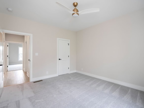 Bright, empty bedroom with neutral walls, carpeted floor, and ceiling fan.