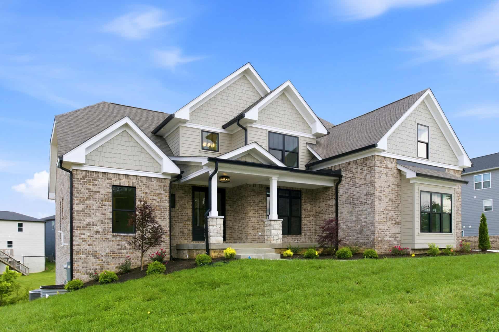 Luxury modern home with brick and siding exterior on a green lawn under blue sky.
