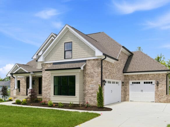 Front view of a modern brick suburban home with beige siding, large black-framed windows, and a two-car white garage under a clear blue sky.