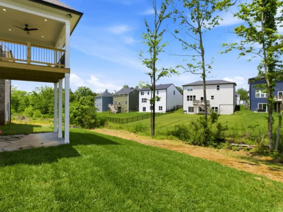 View of modern houses in a green neighborhood with a grassy yard and trees.