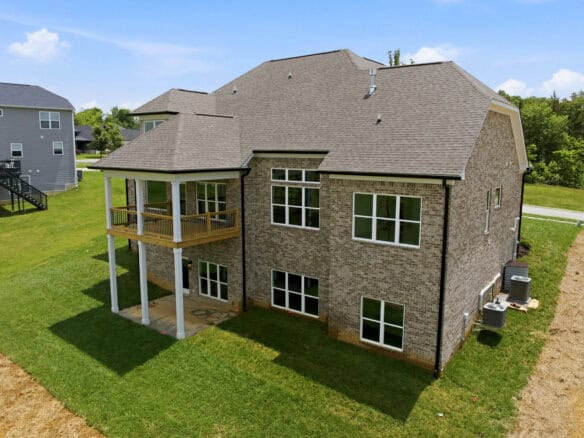 Newly built brick home with a covered porch and multiple large windows in a suburban neighborhood.