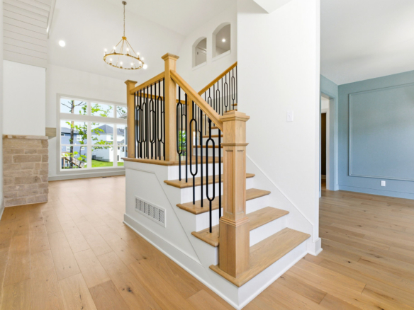 Bright two-story foyer with a wooden staircase, black metal balusters, and a circular chandelier overhead.