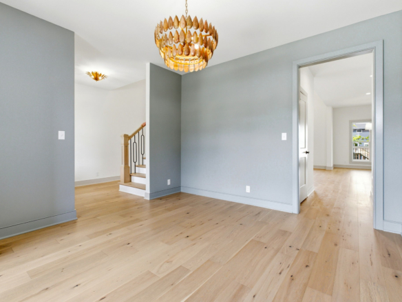 Open entry hall with gray walls, light wood floors, a wooden staircase on the left, and a round gold chandelier above.