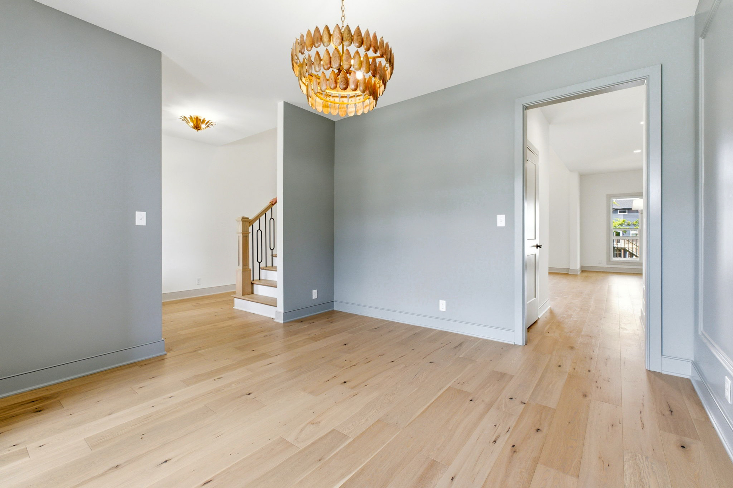 Open entry hall with gray walls, light wood floors, a wooden staircase on the left, and a round gold chandelier above.
