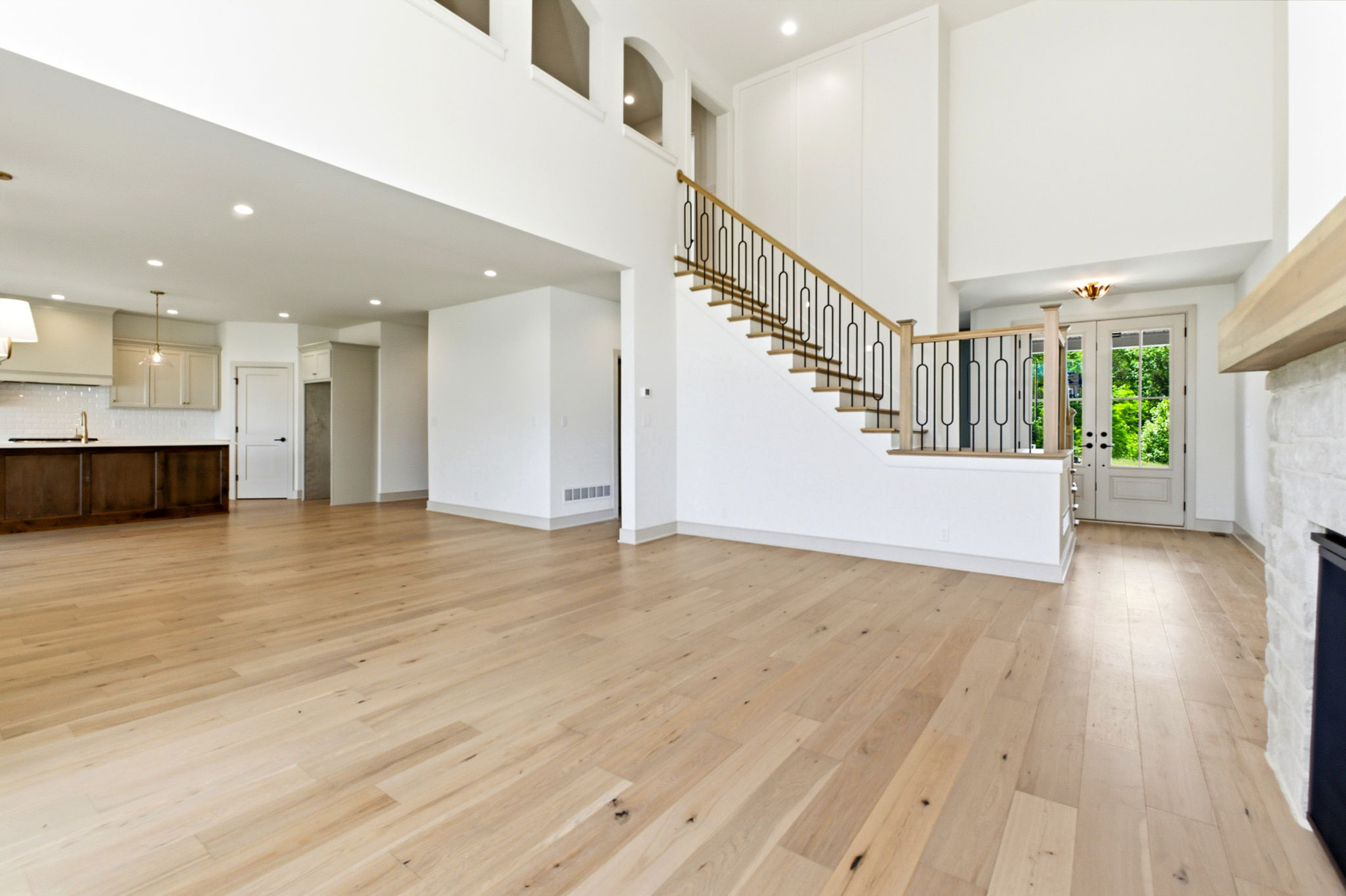 Bright open living space with light wood floors, white walls, and a staircase with decorative black railing near French doors.