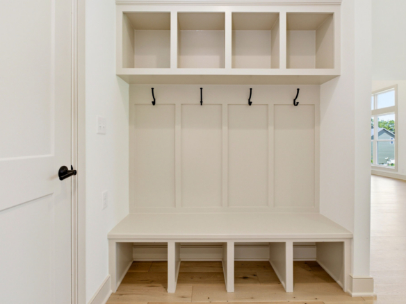 White built-in entryway storage with four upper cubbies, four coat hooks, and a bench above a lower cabinet area.