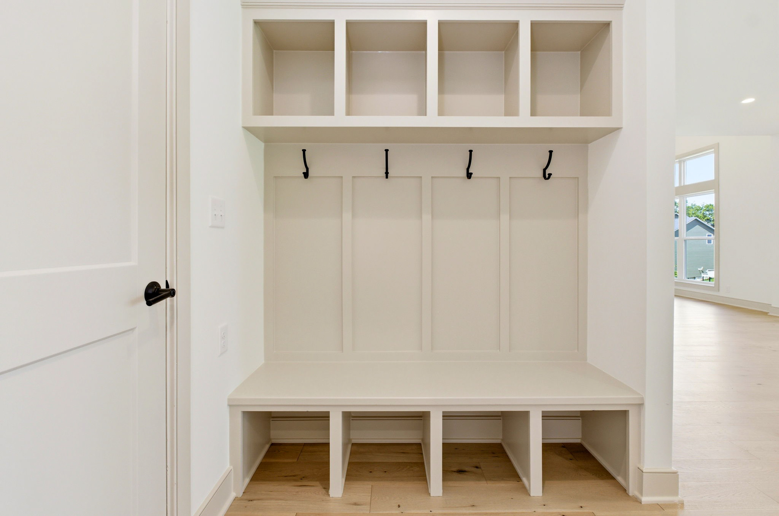 White built-in entryway storage with four upper cubbies, four coat hooks, and a bench above a lower cabinet area.