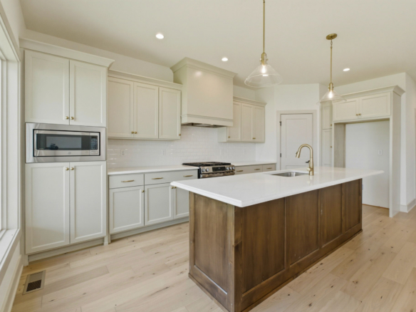 Bright white kitchen with white cabinets, a dark wood island, and glass pendant lights