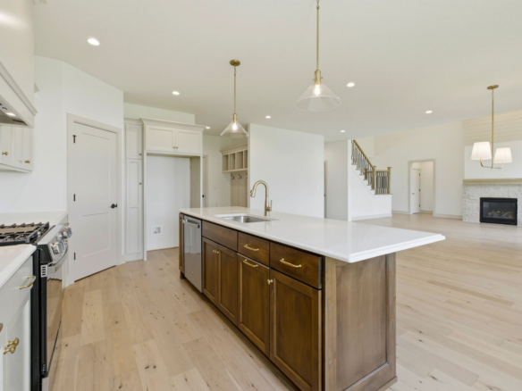 Bright, open-concept kitchen with white cabinetry, a dark wood island, and gold hardware under pendant lights.