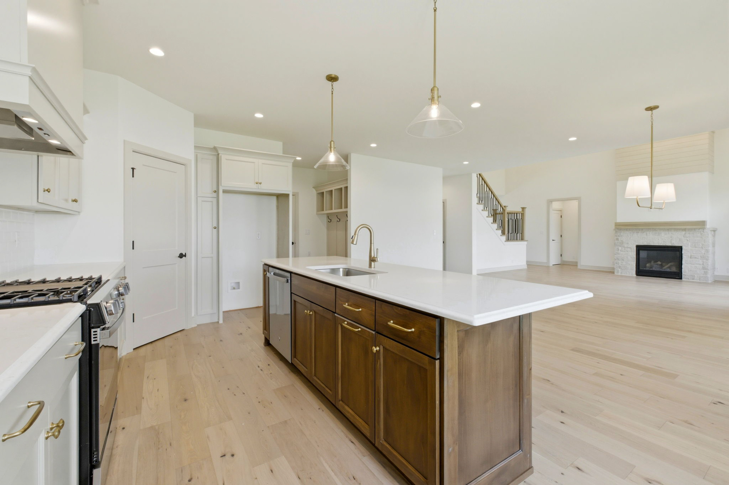 Bright, open-concept kitchen with white cabinetry, a dark wood island, and gold hardware under pendant lights.