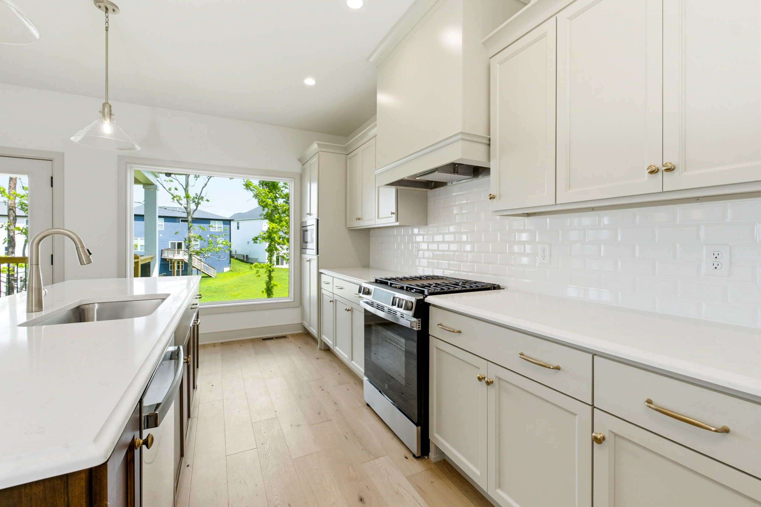 Bright white kitchen with an island, stainless steel stove, and a large window showing a green backyard.