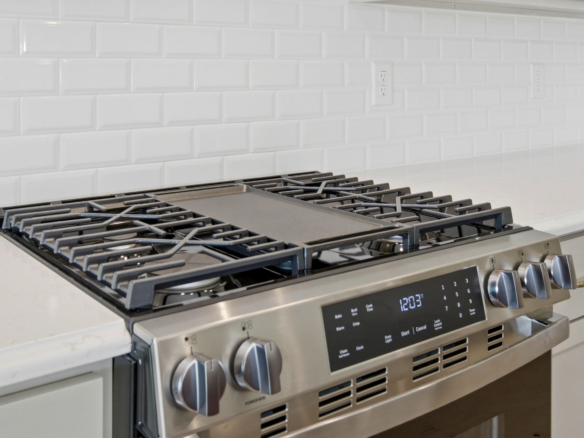 Stainless steel gas range with four burners and control panel against a white subway tile backsplash.