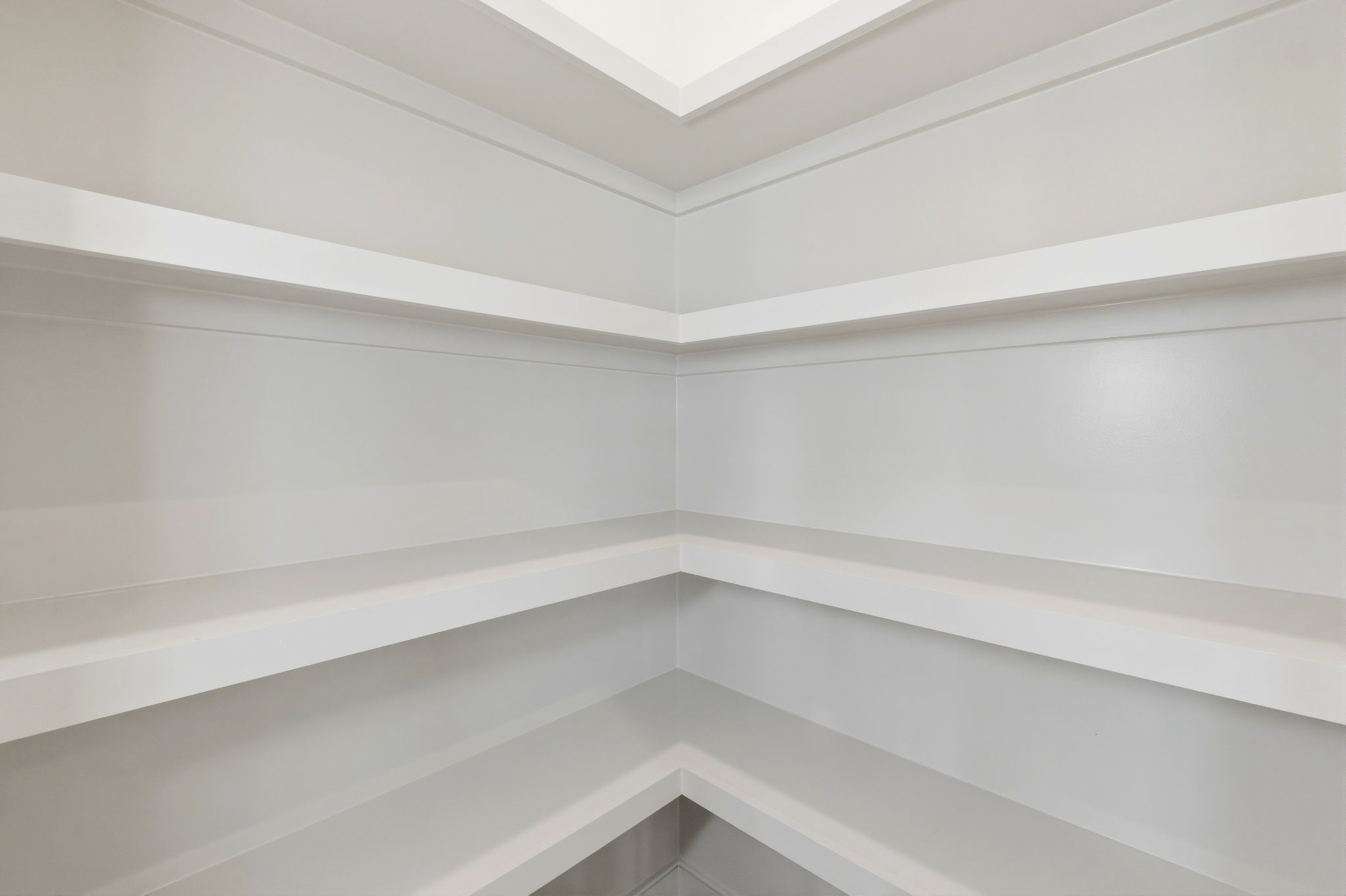 White built-in corner shelving unit with multiple horizontal shelves wrapping around the corner.