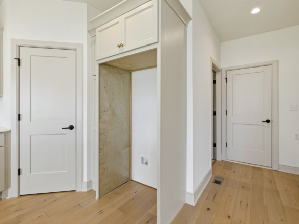 Bright kitchen interior with white cabinetry, light wood floors, and an open pantry alcove between tall cabinets.