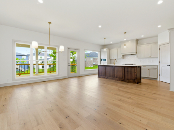 Open-concept kitchen with white cabinets, dark wood island, pendant lights, and large windows overlooking a neighborhood.