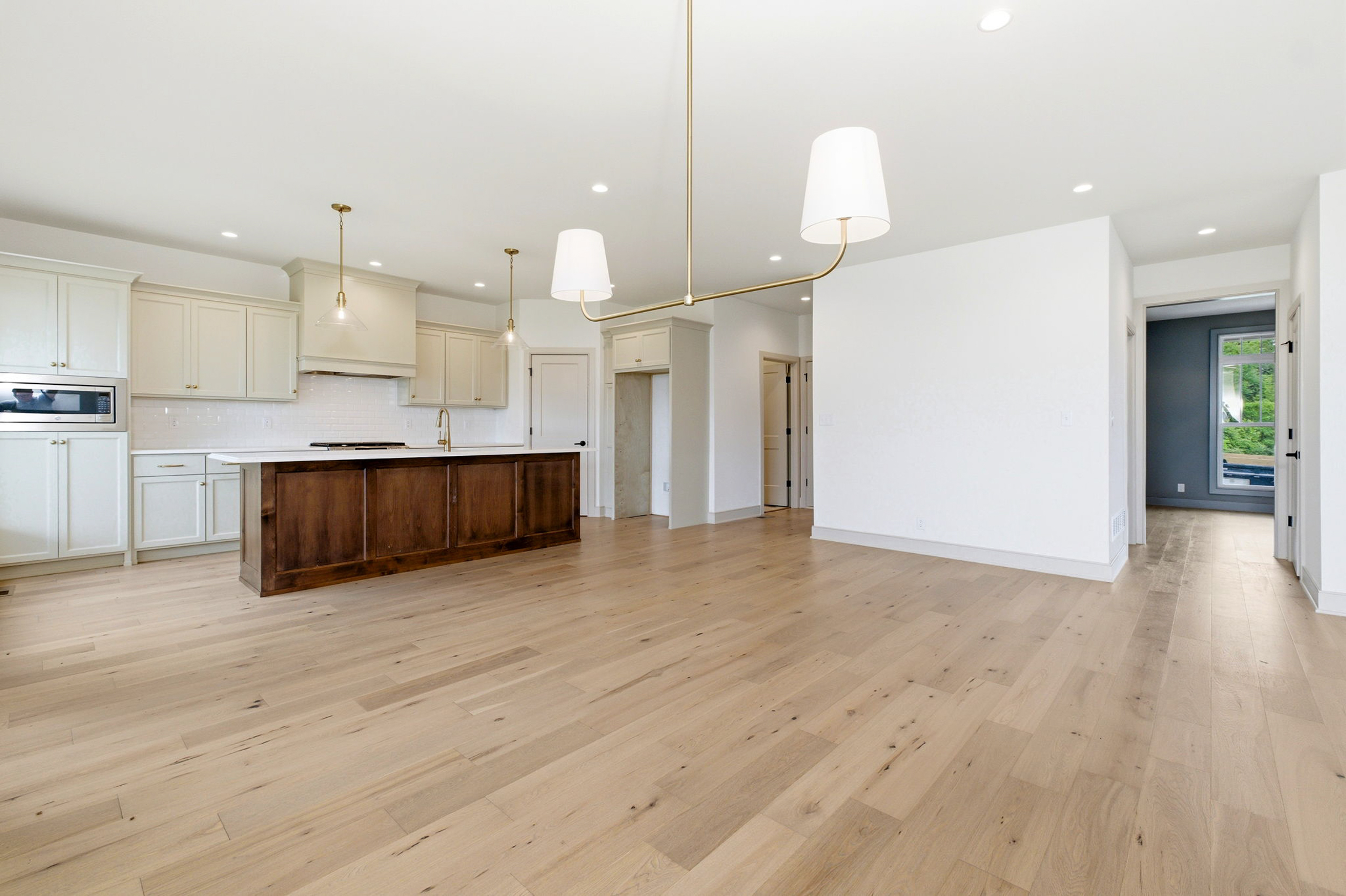 Bright open kitchen with white cabinets, a dark wood island, and brass pendant lights