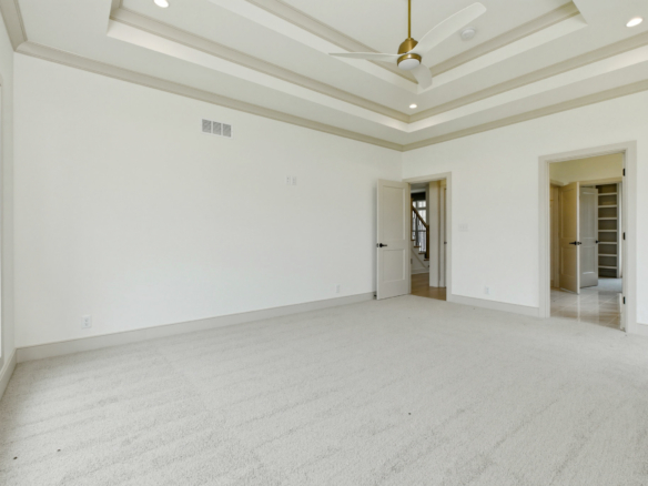 Bright empty living room with white walls, carpet, and a tray ceiling with a ceiling fan; doorway to another room visible on the right.