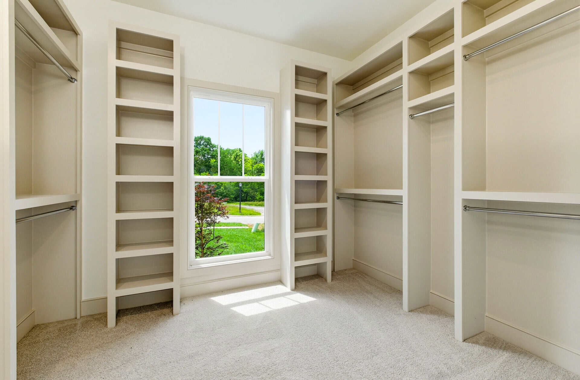 Spacious walk-in closet with built-in shelves and a window overlooking greenery.