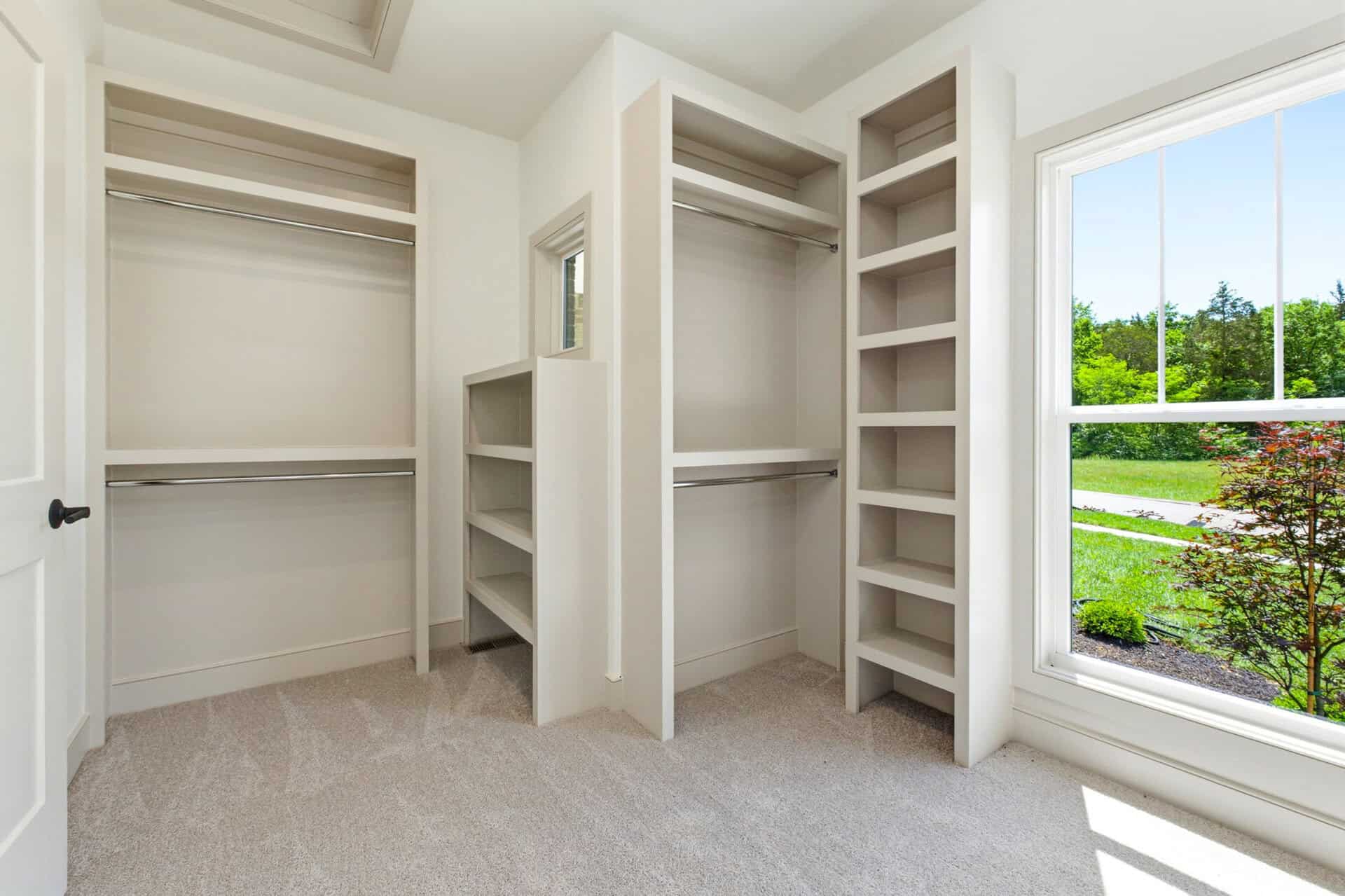 Spacious walk-in closet with built-in shelves and a large window showing greenery.
