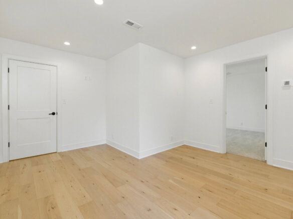 Empty room with white walls and light wood flooring in a new home.