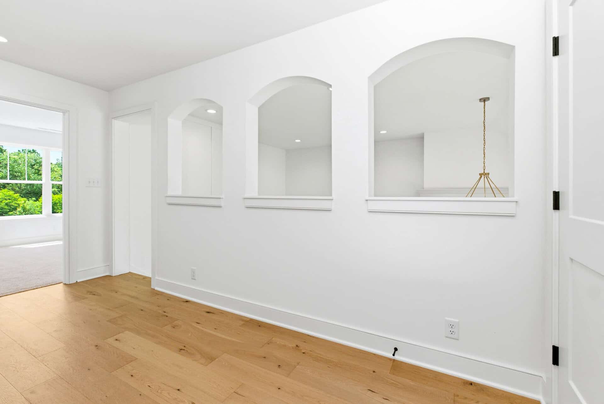 Bright interior with white walls, arched openings, and light wood flooring.