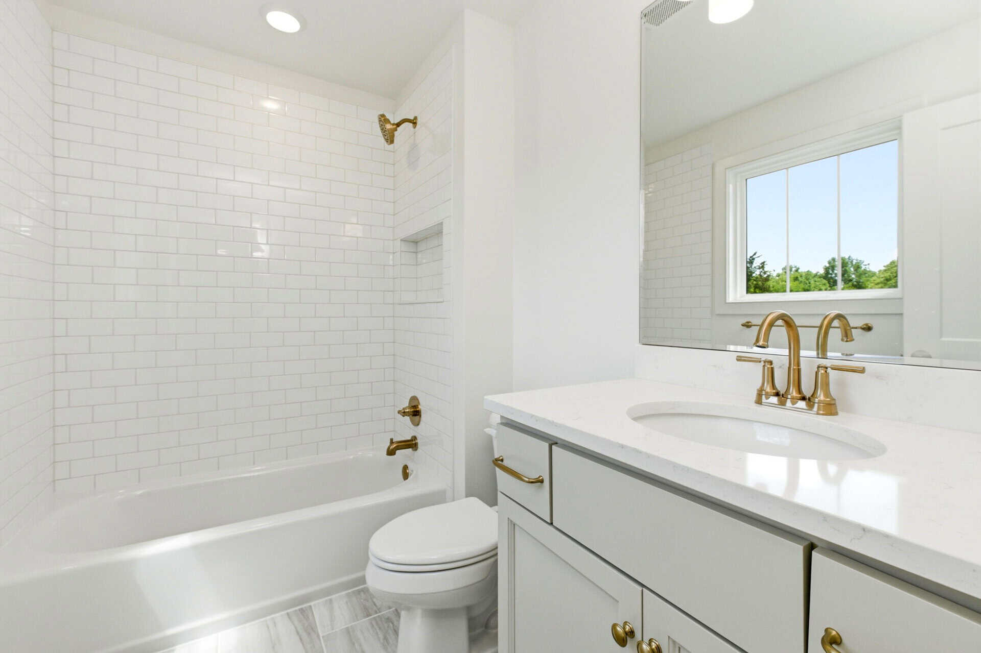 Modern bathroom with white subway tile, gold fixtures, and a large mirror.