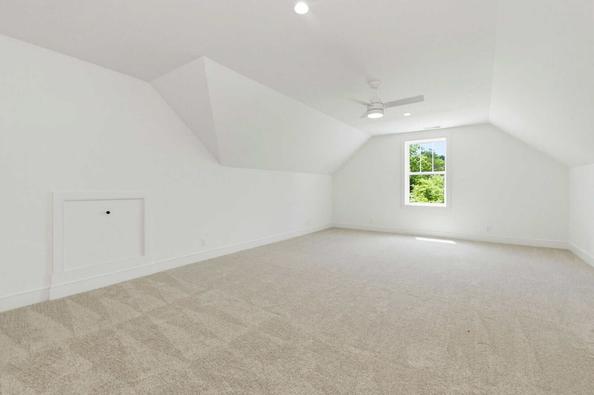 Spacious, bright attic room with white walls, ceiling fan, and window view.