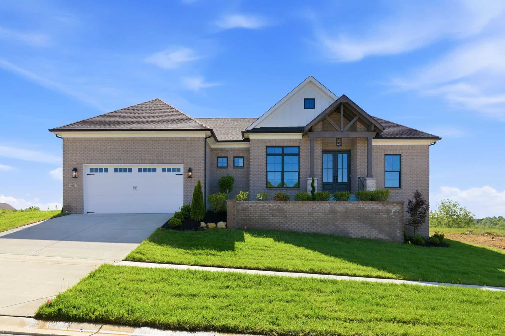 Modern brick home with front porch and well-maintained lawn under blue sky.