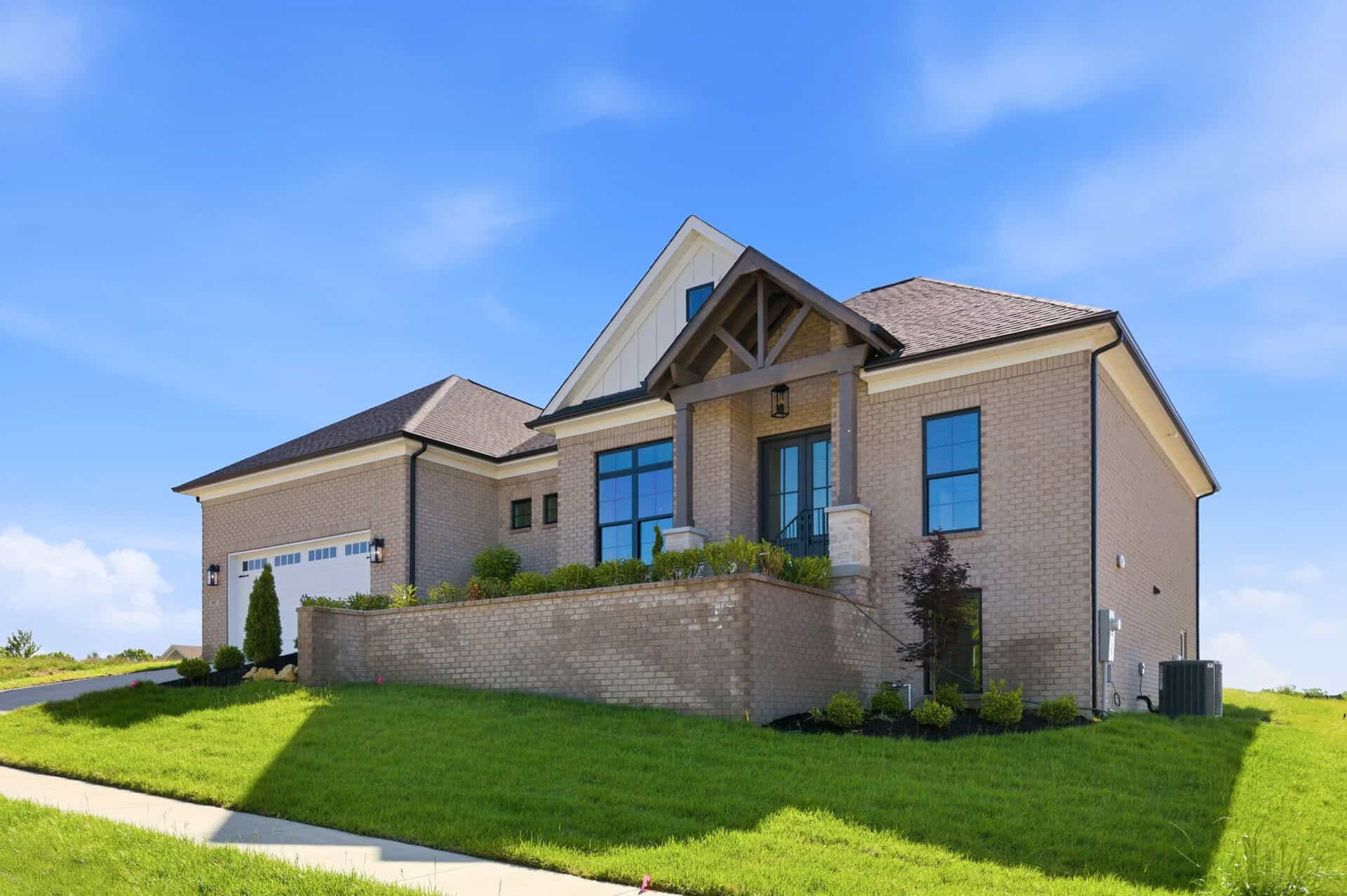 Modern brick two-story house with a gabled roof, front entry, and manicured lawn under a blue sky.