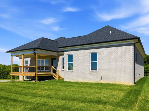 Modern brick home with a porch and a well-maintained lawn under a blue sky.