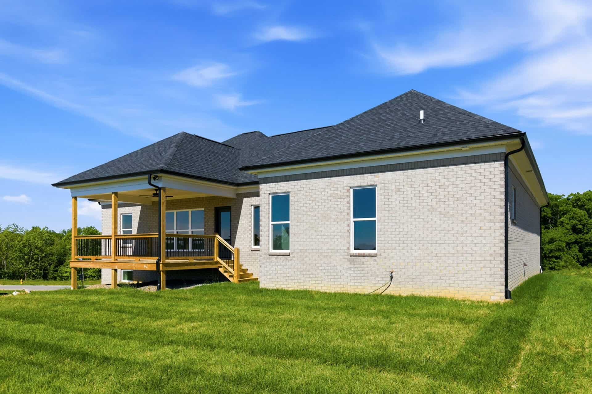 Modern brick home with a porch and a well-maintained lawn under a blue sky.